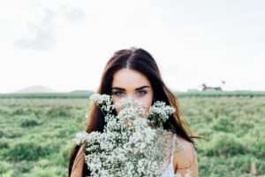 Developing Psychic Abilities woman in a prairie holding white flowers in front of her face with a curious look in her eyes